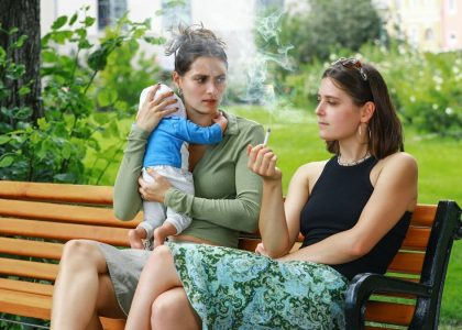 A girl smokes a cigarette on a park bench and disturbs her friend, a young mother and her baby, with her smoke – an appeal for a little more attention and awareness when smoking outdoors. Eine junge Frau raucht auf einer Parkbank eine Zigarette und belästigt mit ihrem Rauch ihre Freundin, eine junge Mutter mit ihrem Baby – ein Aufruf zu etwas mehr Rücksicht und Achtsamkeit beim Rauchen im Freien.